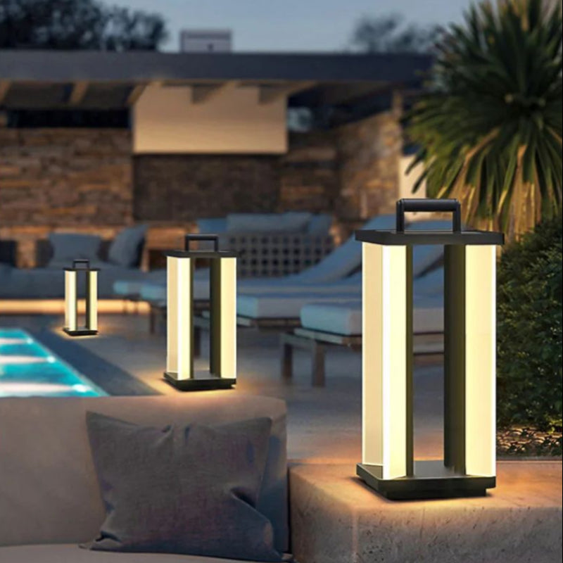 Three illuminated "Villa Solar Lamps" of varying sizes are placed around a modern outdoor lounge area with a swimming pool at dusk or night.