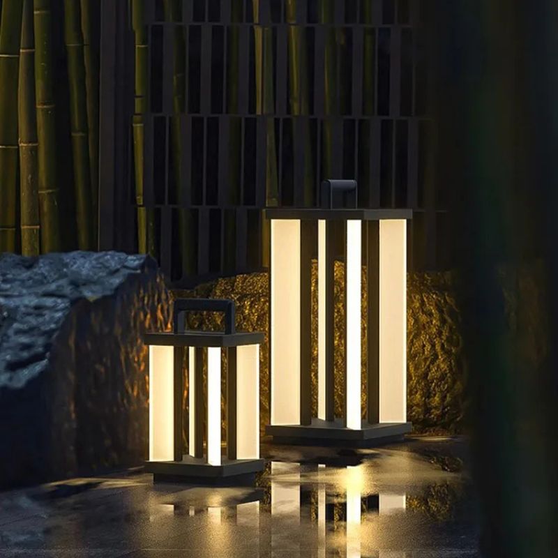 Two illuminated "Villa Solar Lamps" of different sizes stand on a wet, reflective surface at night, with large rocks and a dark, textured background.