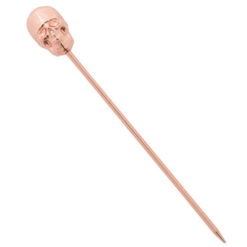 A close-up of a copper-colored cocktail pick with a detailed skull-shaped topper, angled on a solid white background.
