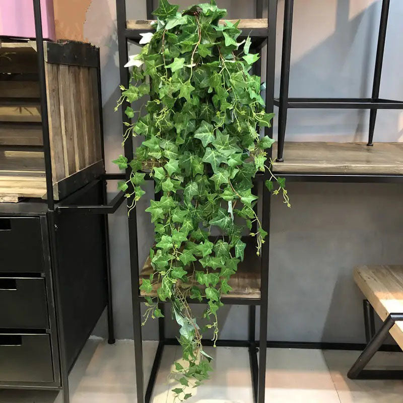 Artificial ivy vine with dense green leaves cascading from a wooden shelf with a black metal frame.