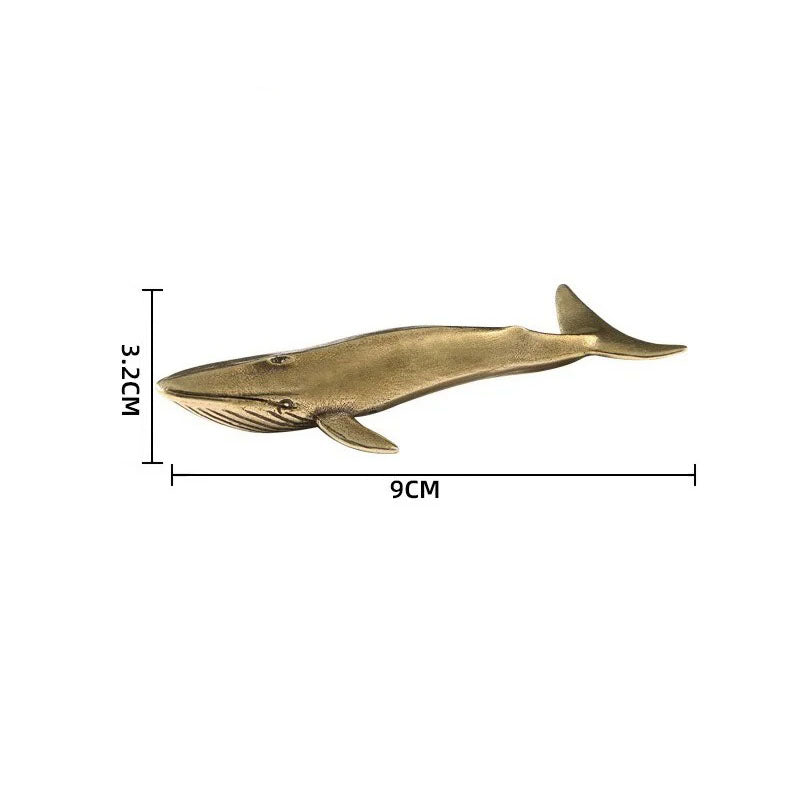 A small, brass-colored whale figurine is displayed on a white background. The figurine's dimensions are marked: 3.2cm in height and 9cm in length.