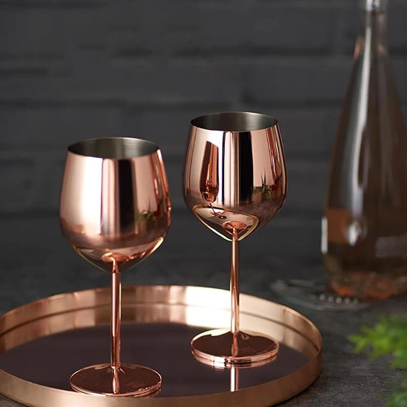 Two rose gold stainless steel wine glasses elegantly displayed on a matching tray against a dark, sophisticated backdrop. A bottle of wine in the background adds to the luxurious and modern ambiance, perfect for stylish entertaining.