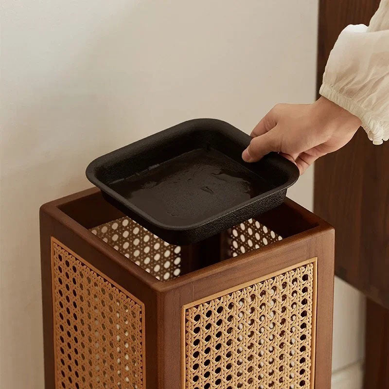 A hand placing a black tray into a wooden umbrella stand with rattan sides.