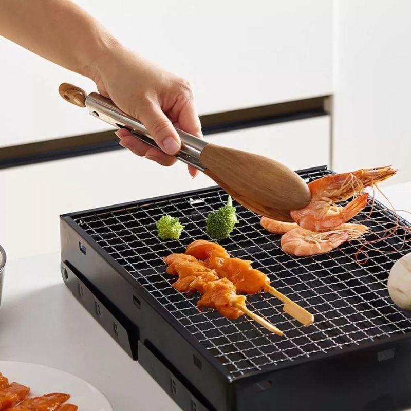 Tongs grilling shrimp and chicken on a small black grill.