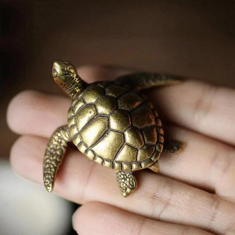 Bronze turtle figurine held in a hand against a blurred background