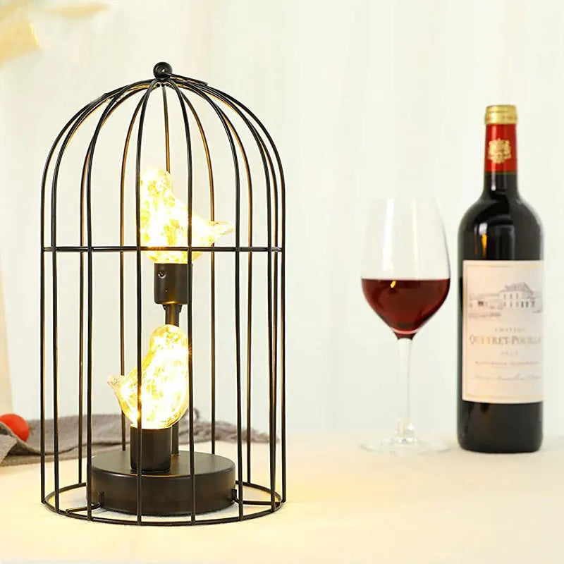 Decorative lamp in a birdcage shape with a wine bottle and glass on a table.