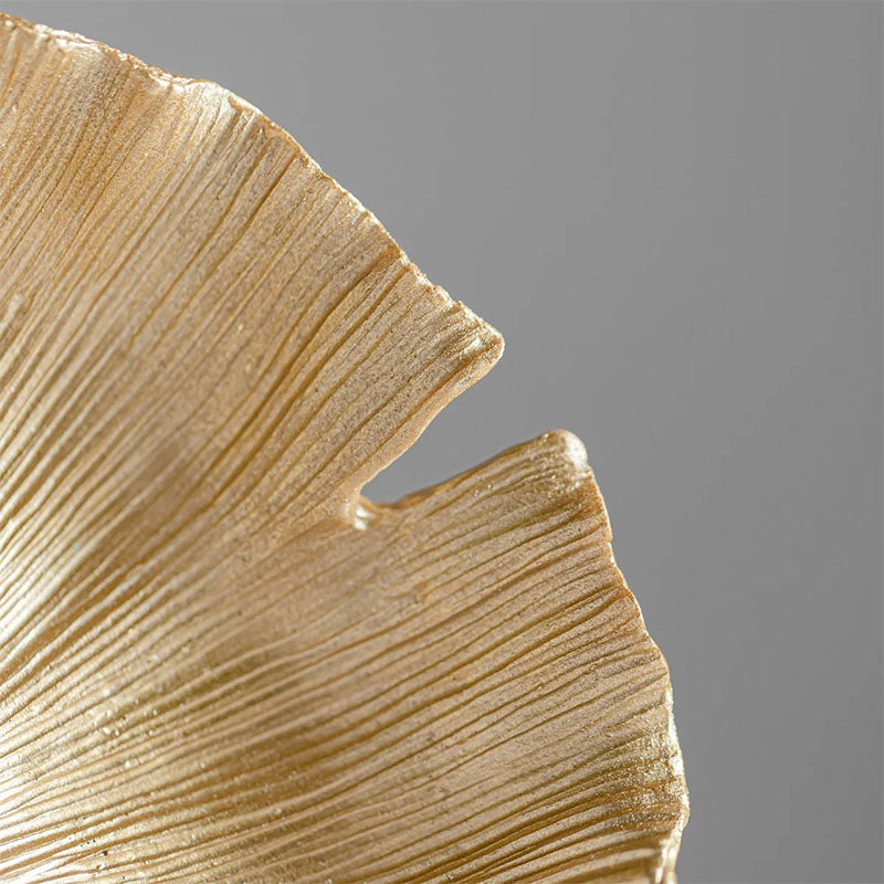 Close-up of the edge of a gold-colored decorative bowl, showcasing its organic, ginkgo leaf-inspired shape with fine, textured grooves.