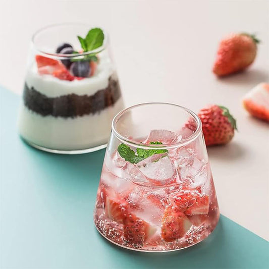 Two glasses, one with a layered dessert and the other with a strawberry drink, with fresh strawberries nearby.