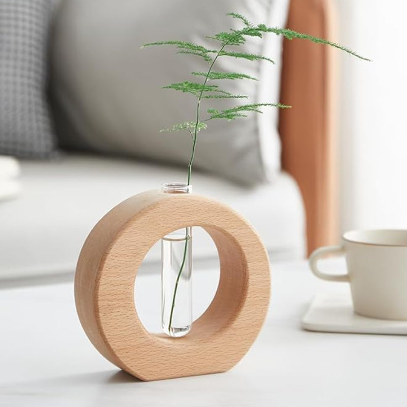 A circular wooden vase with a clear glass test tube holds a leafy green stem.