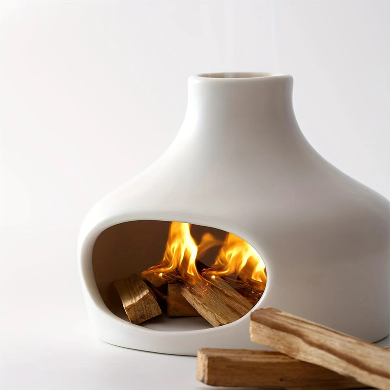 A white ceramic incense burner with a hollow opening, holding burning palo santo wood with visible flames, against a clean white background.