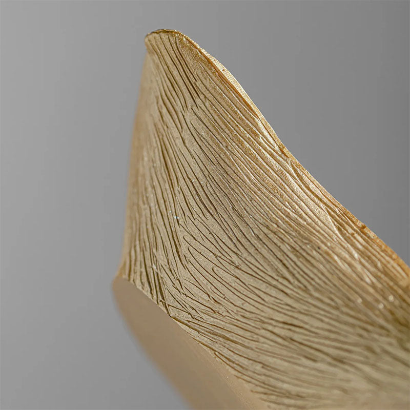 Close-up of a gold-colored decorative bowl, highlighting the intricate vein-like texture and fine details of the ginkgo leaf design.