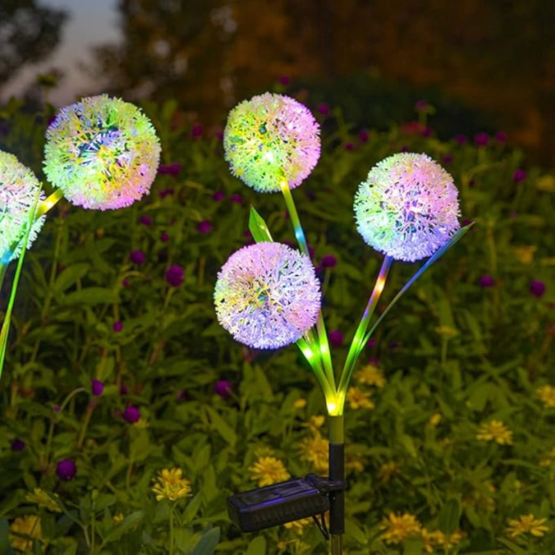 Four multicolored solar dandelion lights illuminate a garden at night.