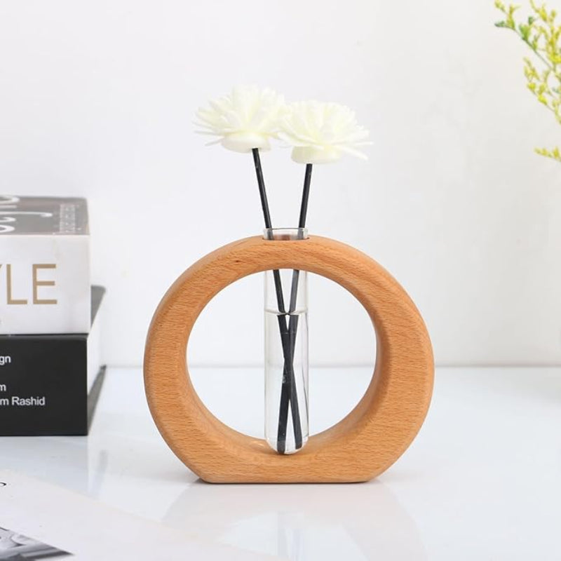 A light wooden circular vase holds a clear glass test tube with two artificial white flowers.