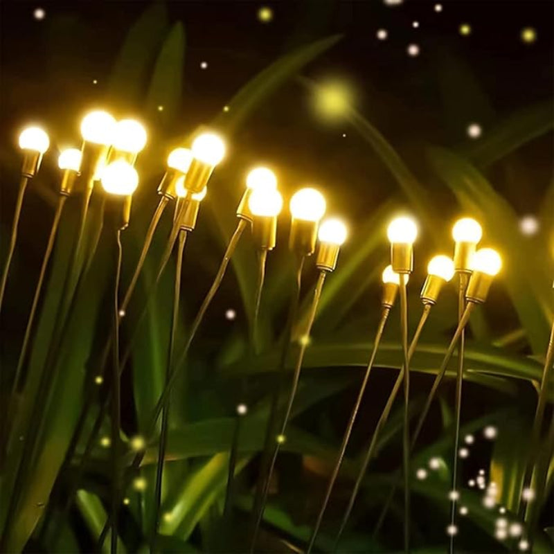 Several slender stems with warm white spherical lights at their tips rise from dark green foliage against a dark night sky dotted with small white and yellow specks, resembling stars or fireflies. The lights create a whimsical and magical garden scene.