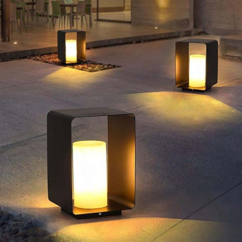 Three modern, dark rectangular outdoor pathway lights with glowing cylindrical diffusers, illuminating a stone patio area at dusk.