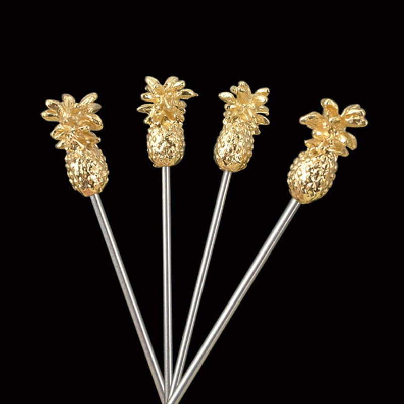 Close-up of four stainless steel cocktail picks with detailed gold pineapple-shaped toppers, arranged in a splayed formation against a solid black background.