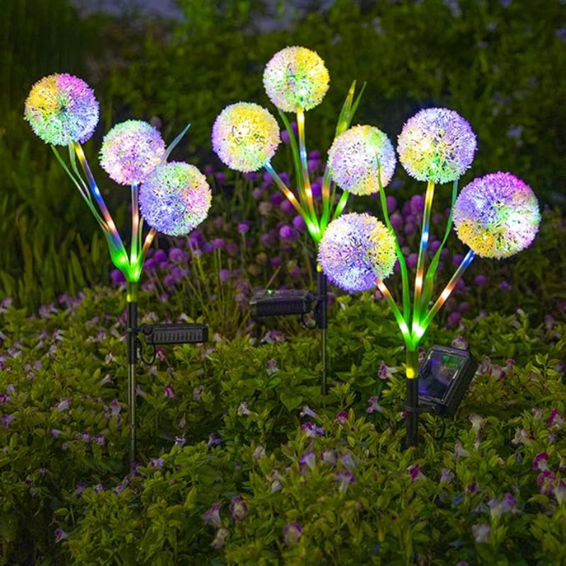 Several colorful solar dandelion lights in a garden at night.