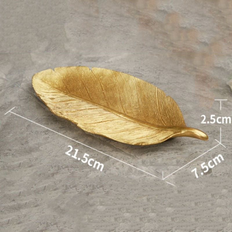 A gold, leaf-shaped dish on a gray textured surface, with dimension labels.