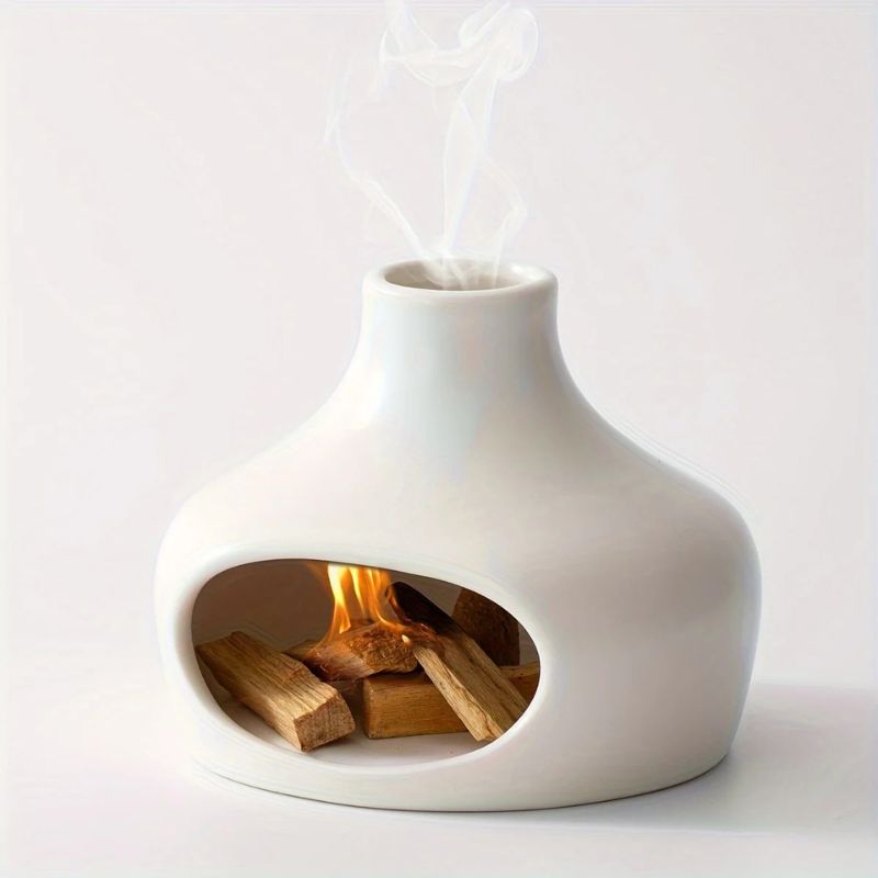 A white ceramic incense burner with an open chamber containing burning wood, emitting smoke through the top opening.