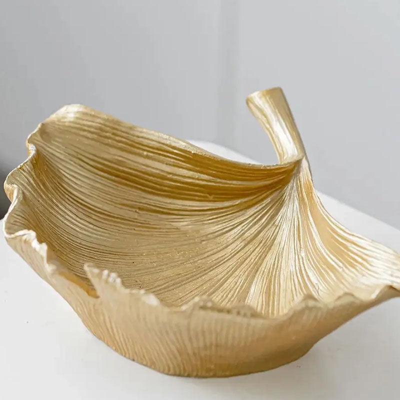 Close-up of a gold-colored decorative bowl with a textured ginkgo leaf design, placed on a white surface.