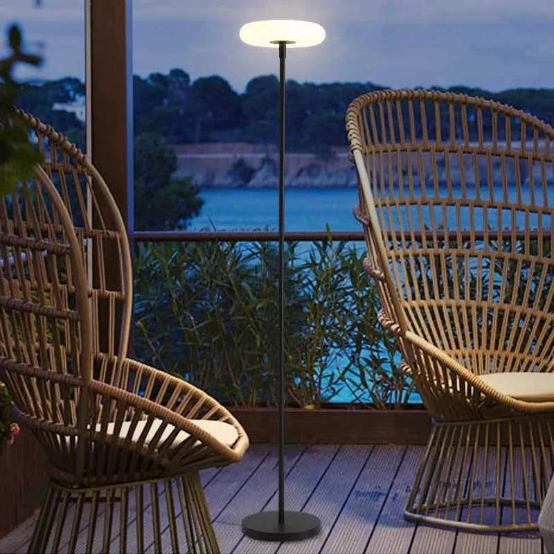 Two wicker chairs on a deck with a standing lamp and a scenic view of water and trees.