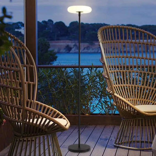 Two wicker chairs on a deck with a standing lamp and a scenic view of water and trees.