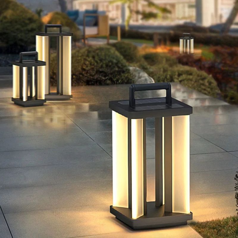 Three illuminated "Villa Solar Lamps" of varying sizes stand on a paved outdoor surface at night, with blurred greenery and distant lights in the background.