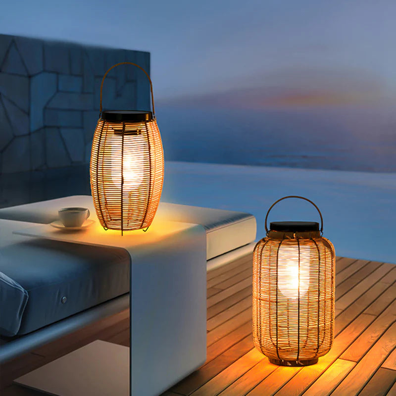 Two warm-toned, cylindrical outdoor lanterns made of vertical slats emit a soft glow as they sit on a surface. The lanterns have handles for hanging.