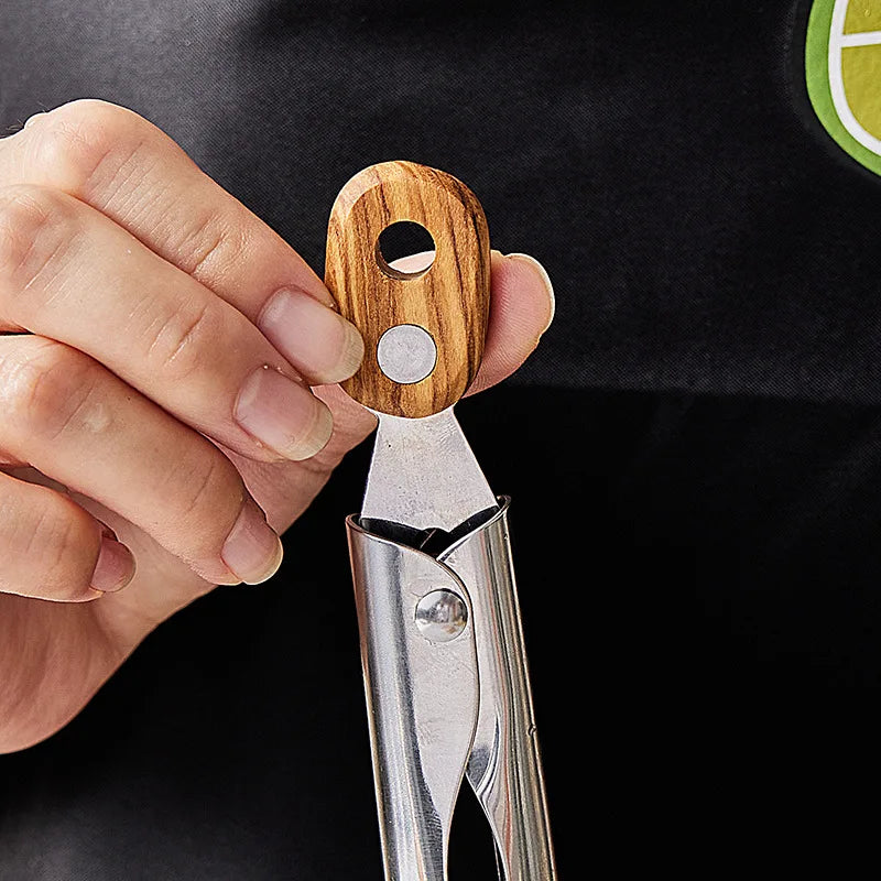 Close-up of a person's hand adjusting the locking mechanism on a pair of stainless steel tongs with a wooden handle. The handle has a round hole and a silver button.