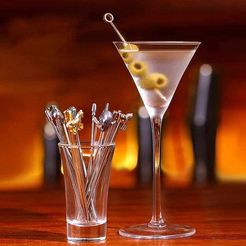 A martini in a stemmed glass with olives and a cocktail pick, alongside a glass filled with assorted metal cocktail picks.