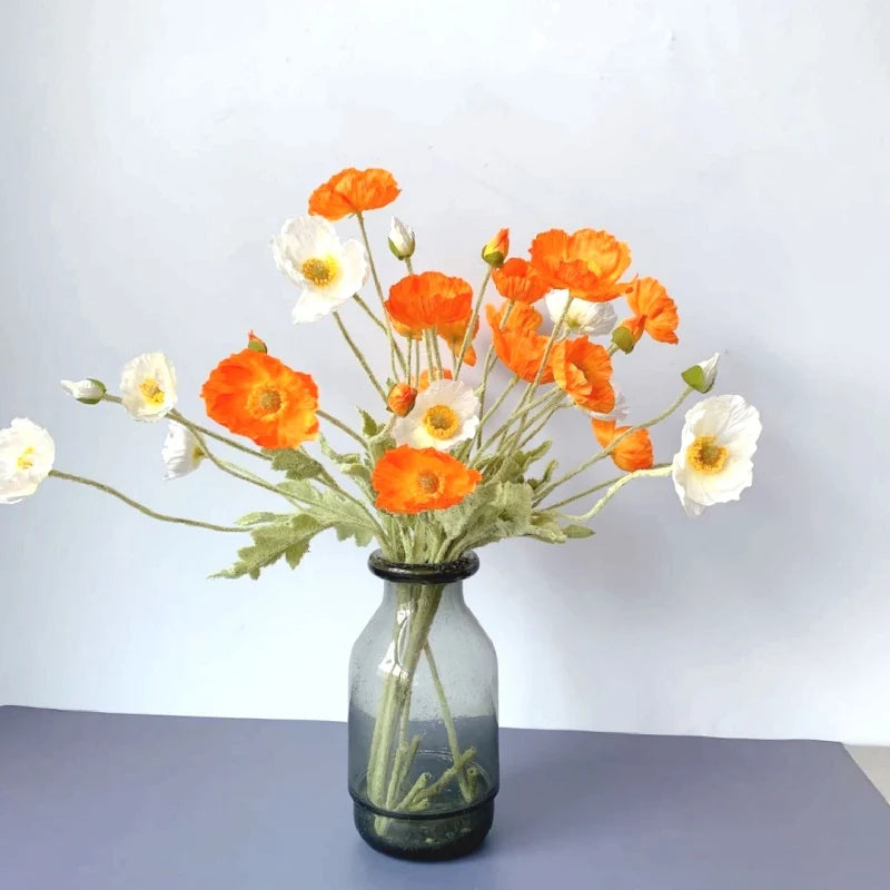 A gray vase holds a bouquet of orange and white poppies.