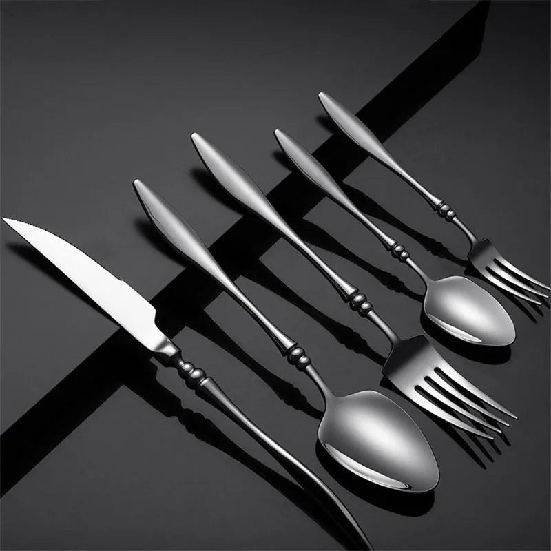 A set of six dark silver utensils on a black surface.
