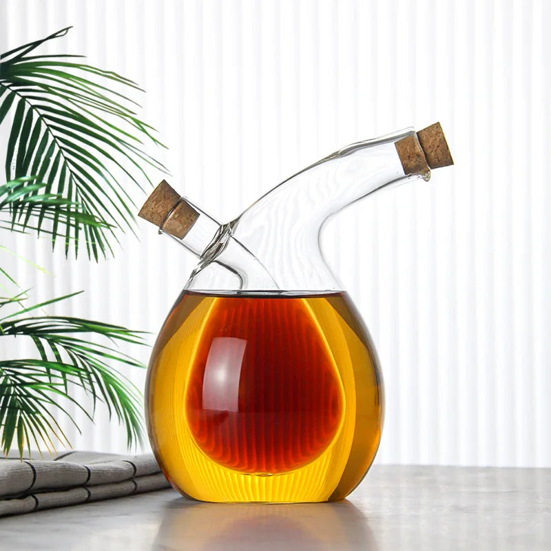 Glass decanter with cork stopper containing a layered liquid on a light surface with a plant in the background.