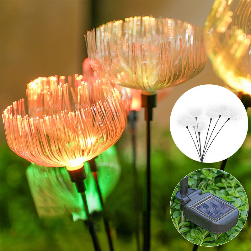 Close-up of several solar-powered garden lights with a jellyfish-like fiber optic design emitting warm orange and green glows. Inset images show the light's structure and a solar panel base.