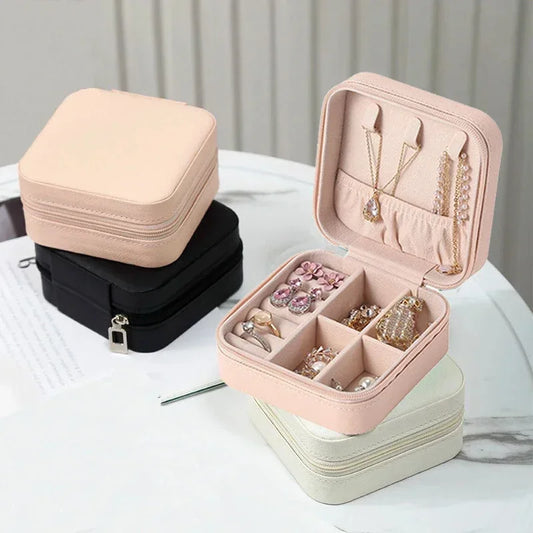 A collection of small, square, zippered jewelry boxes in black, pink, and white, with one pink box open to display various pieces of jewelry.