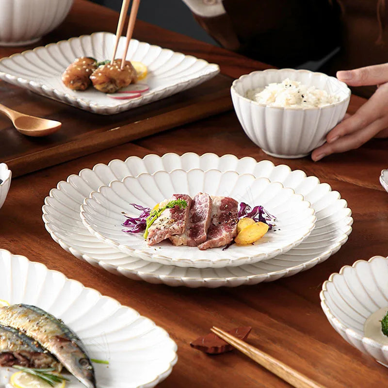 A set of white, scalloped-edge ceramic dinnerware with vertical ridges, featuring various plates and bowls with food on a wooden table.