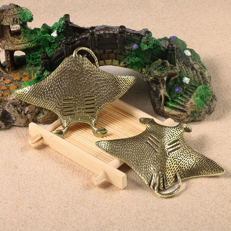 Gold manta ray figurines on a sandy surface with a decorative aquarium background.