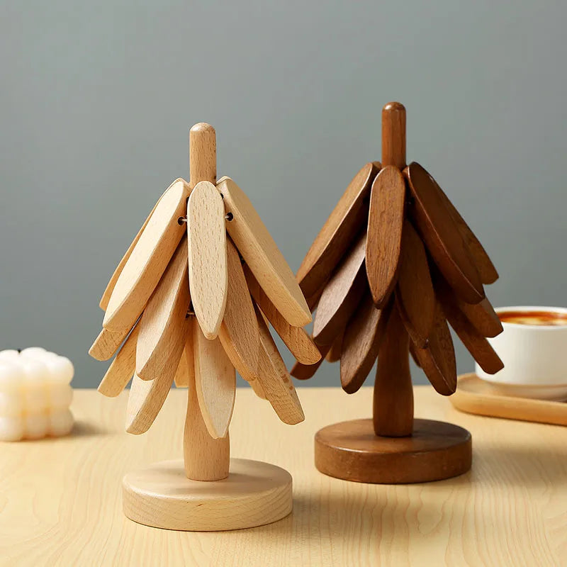 Two tree-shaped wooden trivets, one light and one dark, on a light wooden table. A candle and mug are visible in the background.