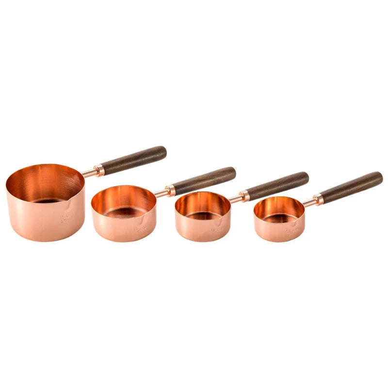 A set of four copper-toned stainless steel measuring cups with dark wooden handles is arranged in a row from largest to smallest against a white background.