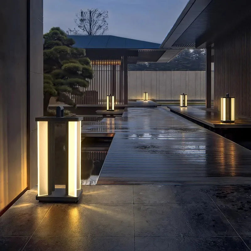 Several illuminated "Villa Solar Lamps" line a wet stone pathway and wooden deck alongside a reflecting pool in a modern outdoor setting at dusk or night.