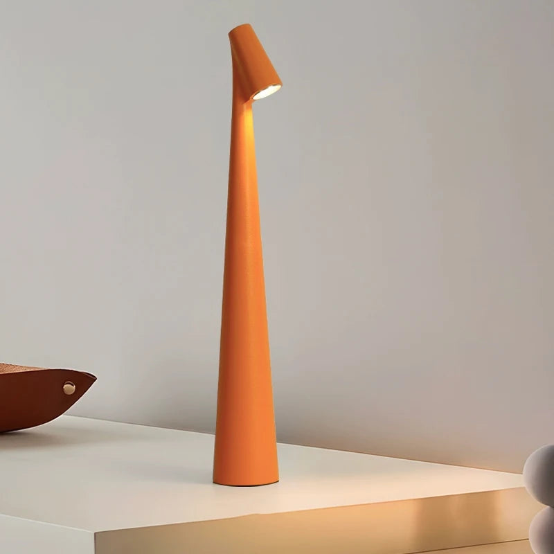 A sleek, modern, orange lamp with a narrow, tall base and a small light at the top, standing on a white surface.
