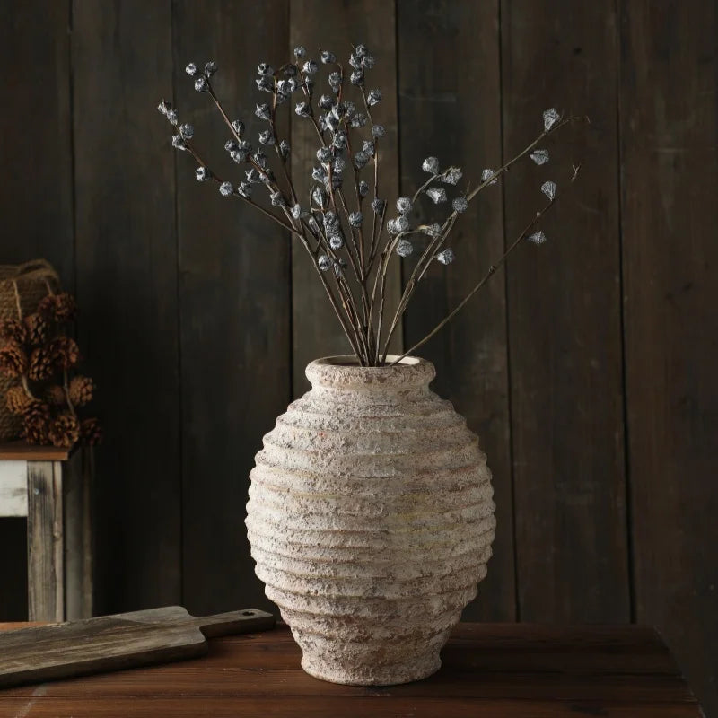 A rustic, heavily textured ceramic vase with dried blue-grey eucalyptus seed pods on a dark wooden table.