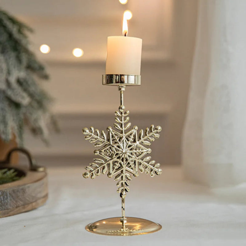Lit candle in a gold snowflake-shaped candle holder on a white surface.