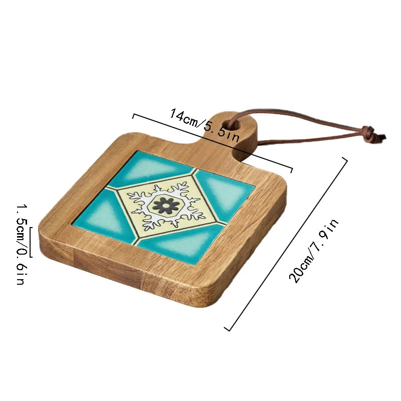 A wooden trivet with a ceramic tile inlay featuring a blue and white geometric floral design is displayed. The trivet has a handle with a hole and a brown leather loop for hanging. Dimensions are labeled: 20 cm (7.9 in) in length, 14 cm (5.5 in) in width, and 1.5 cm (0.6 in) in thickness.