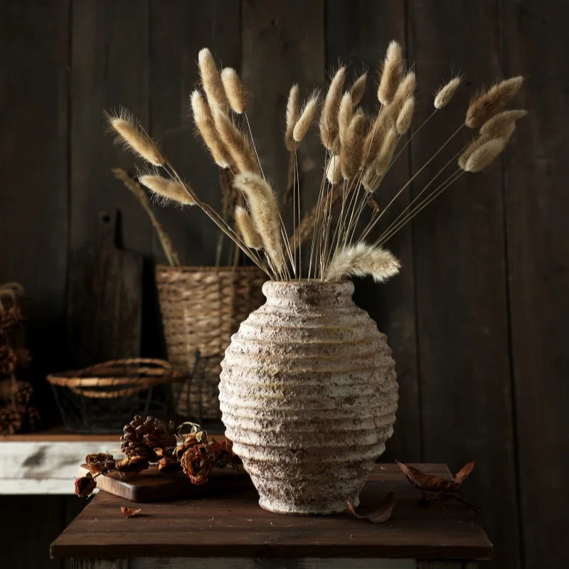 Rustic, textured terracotta vase with dried bunny tail grass on a dark wooden table.