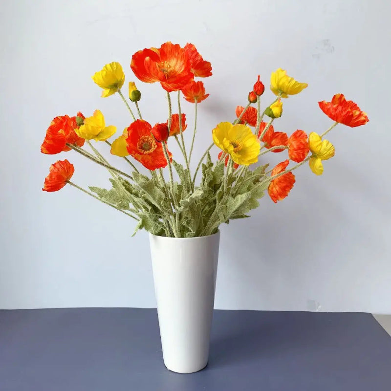 A white vase holds a bouquet of red and yellow poppies.