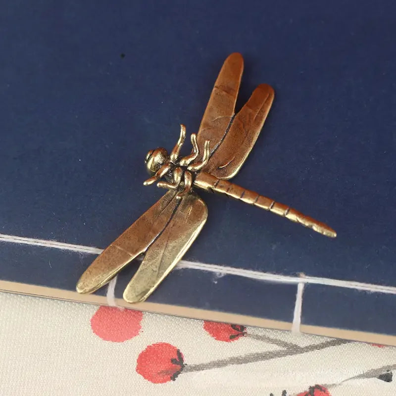 Bronze dragonfly figurine on a blue surface with floral patterned fabric underneath