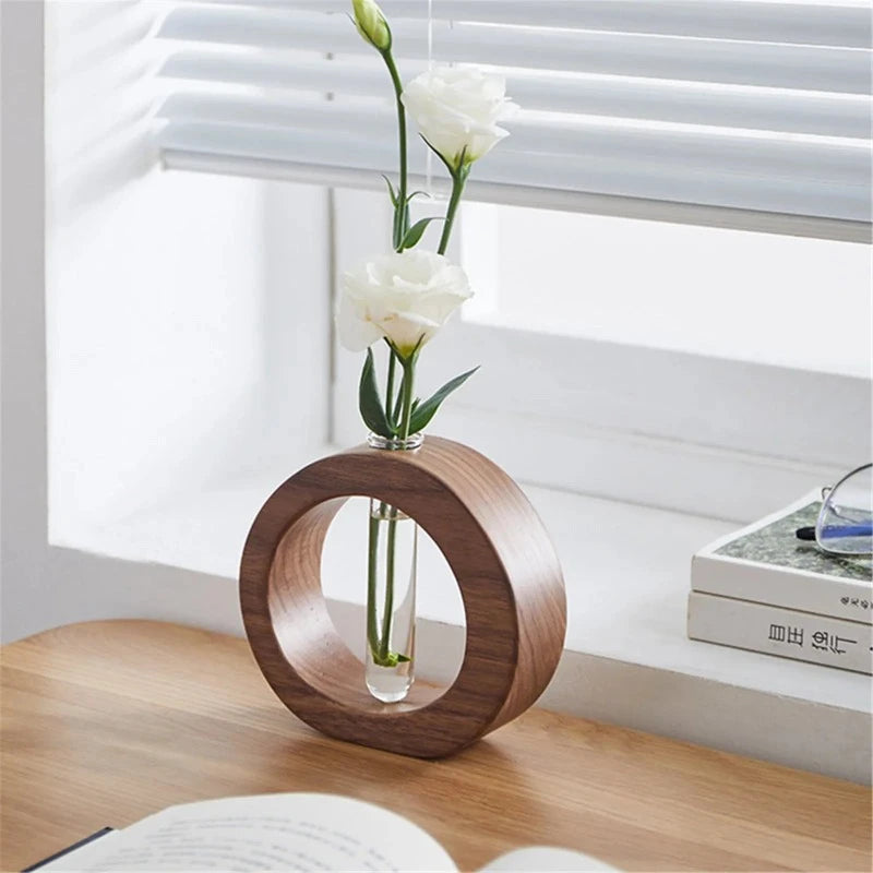 A dark wooden circular vase holds a clear glass test tube with two white lisianthus stems and buds.