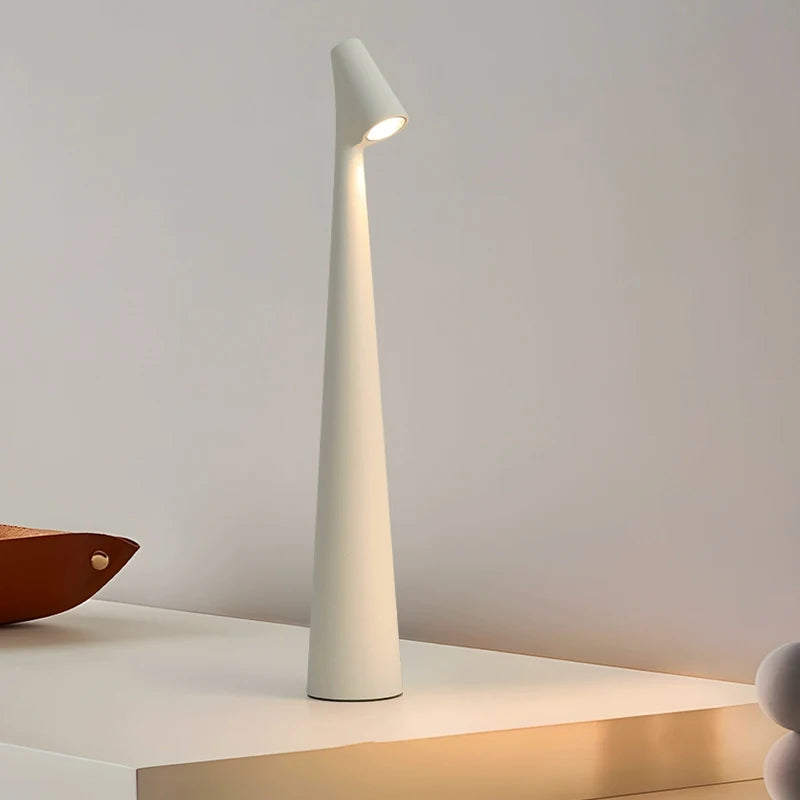 A sleek, modern, white lamp with a narrow, tall base and a small light at the top, standing on a white surface.