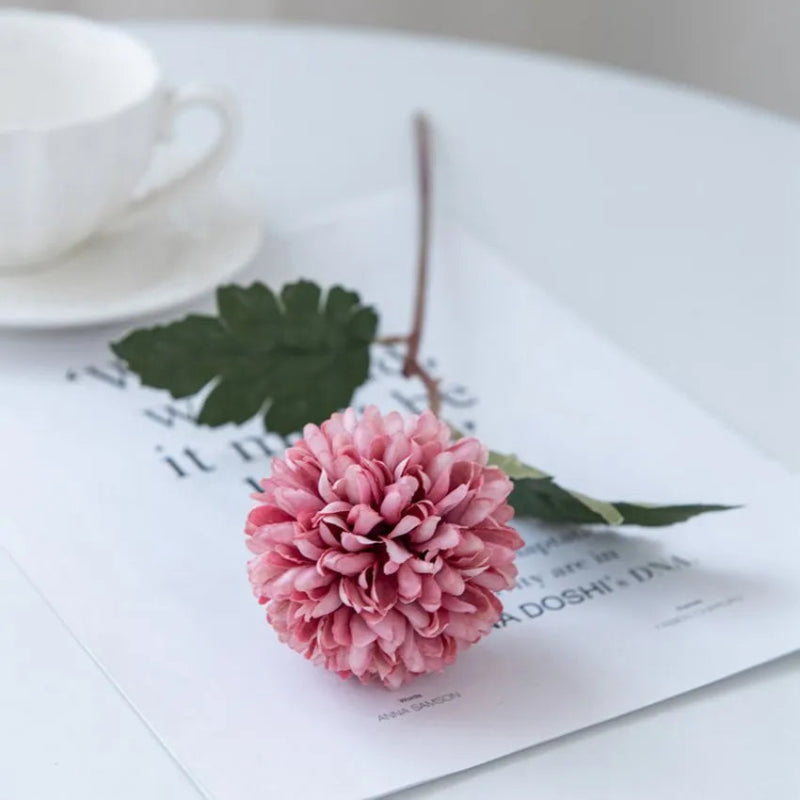A single pink chrysanthemum flower on a white table with a cup.